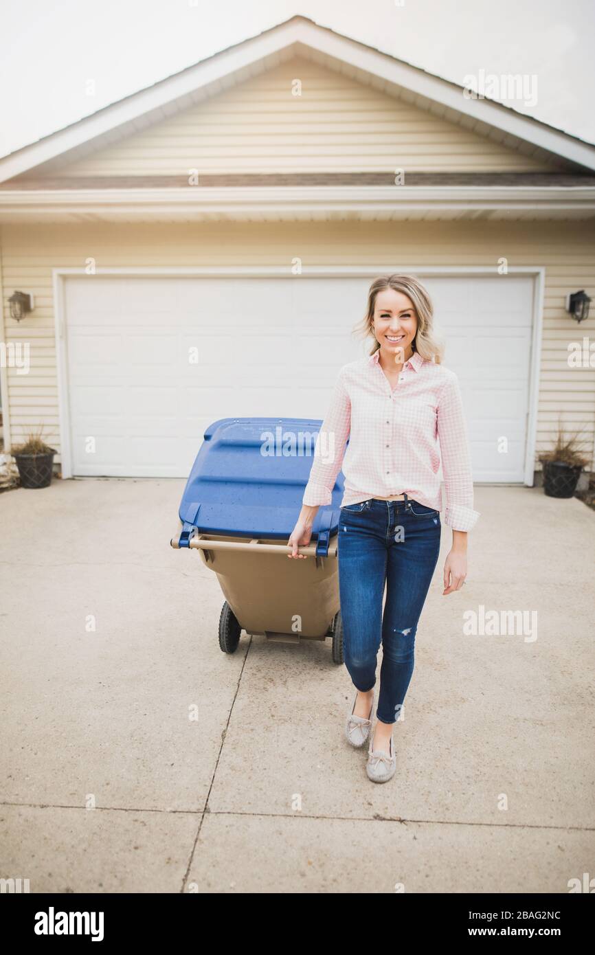 Young woman pulling garbage can down driveway Stock Photo Alamy
