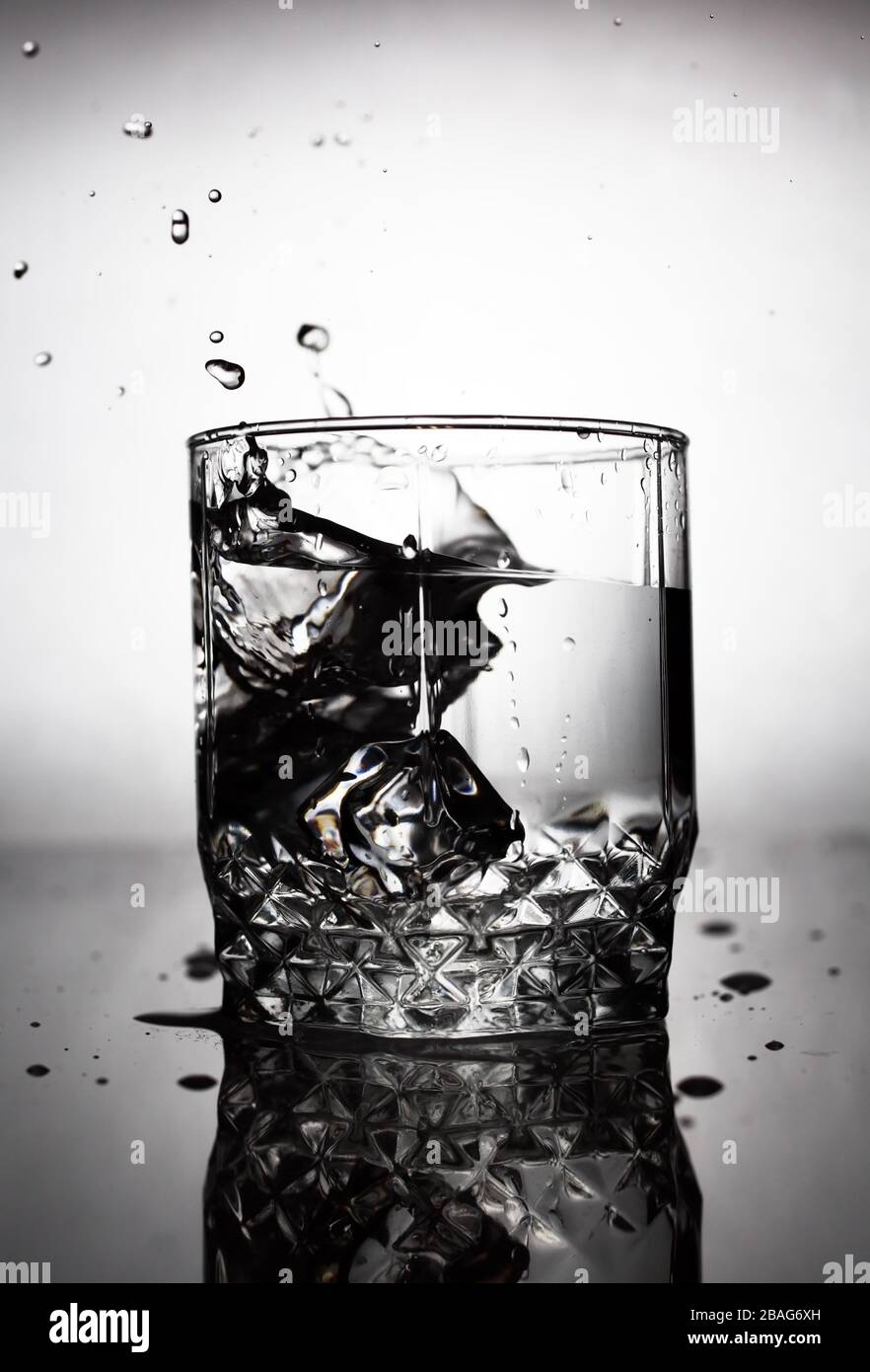 an ice cube is thrown into a glass of water, water splashes fly from a ...