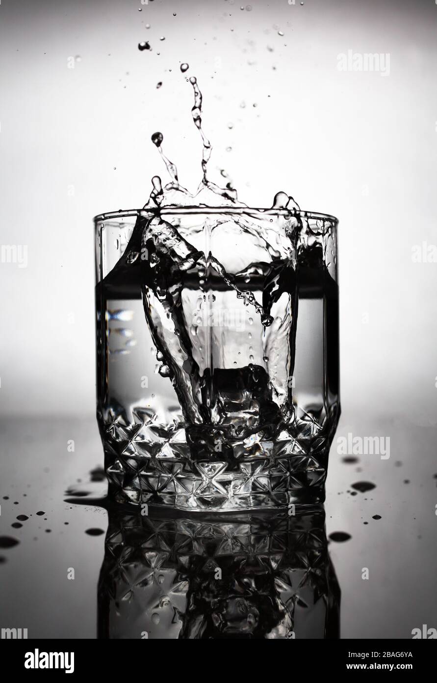 an ice cube is thrown into a glass of water, water splashes fly from a ...