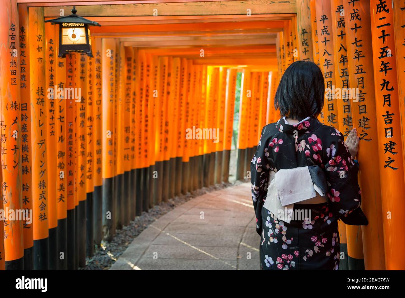 Women in kimono stand at Red Torii gates in Fushimi Inari shrine, one of famous landmarks in Kyoto, Japan Stock Photo