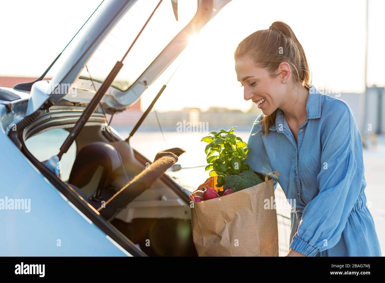 Young woman in car park, loading shopping into boot of car Stock Photo
