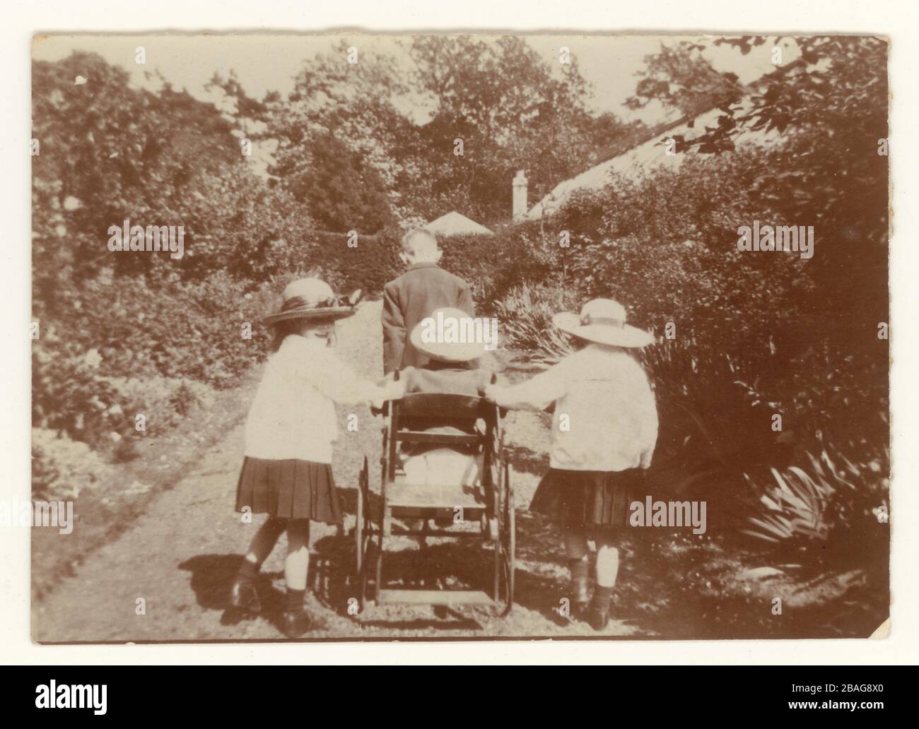 Early 1900's photograph of children pushing a wheelchair in a walled garden, U.K., circa 1910. Stock Photo