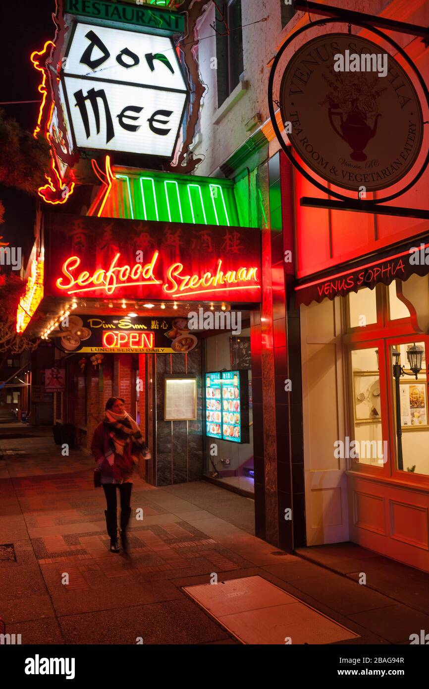 Single woman walking by Chinese restaurant in Chinatown at night-Victoria, British Columbia, Canada. Stock Photo