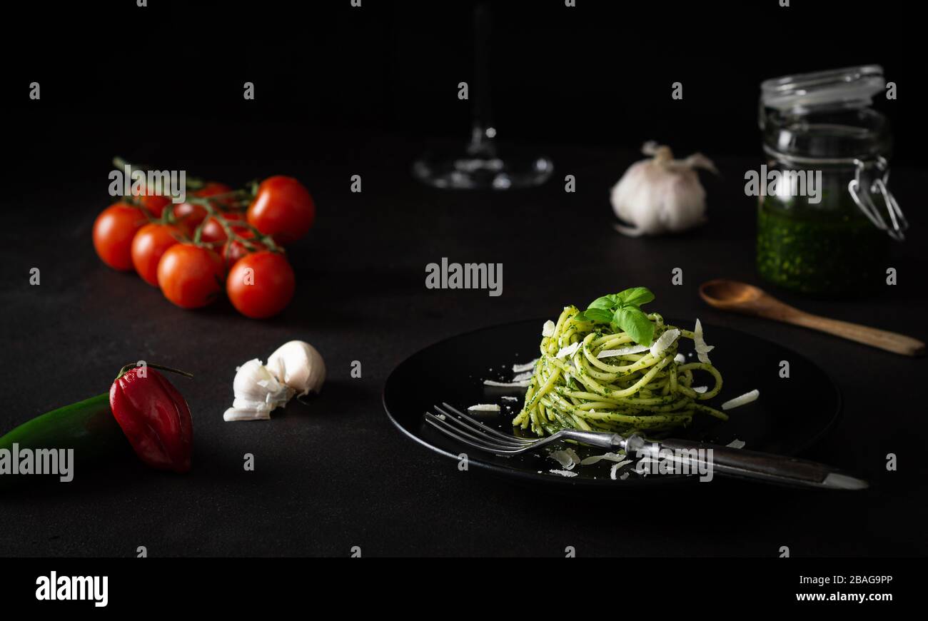 Spaghetti with pesto sauce with green Genoese sauce with fresh tomatoes on black plate and black background with side light Stock Photo