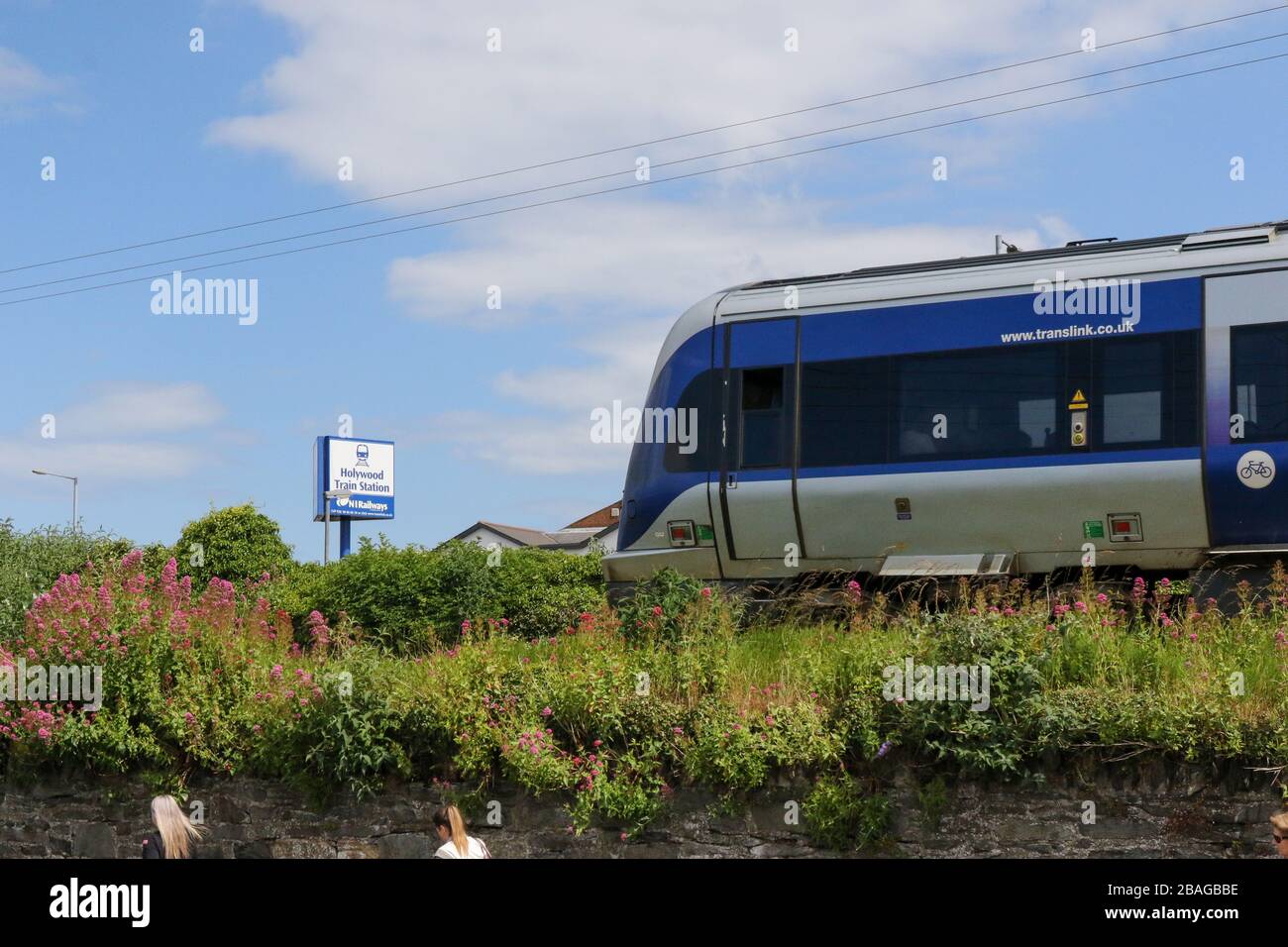 NIR Translink commuter CAF train leaving Holywood Station in County Down. with disembarked passengers walking alongside the railway embankment. Stock Photo