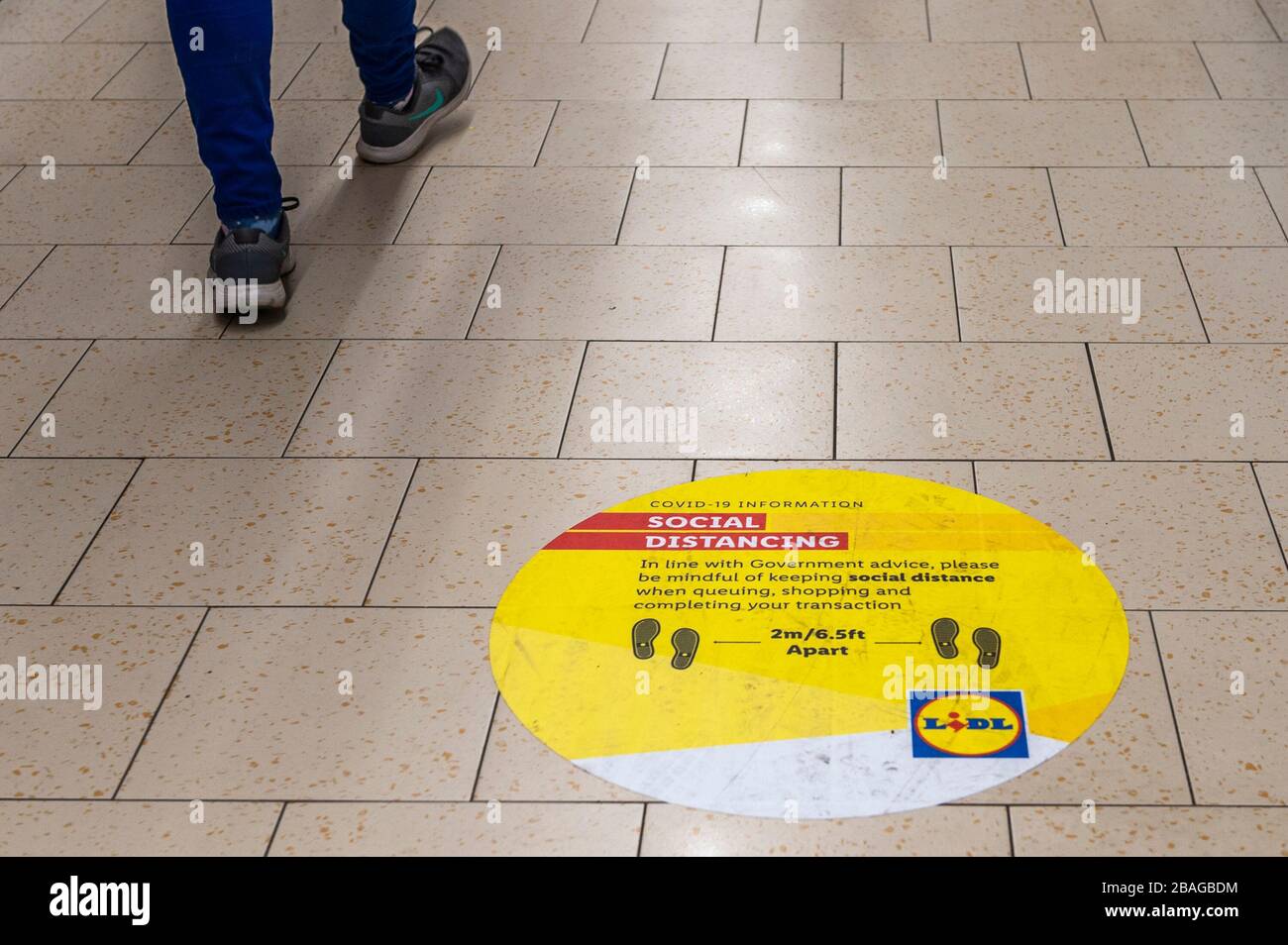 Clonakilty, West Cork, Ireland. 27th Mar, 2020. A woman walks past a social distancing sign in Lidl Supermarket, Clonakilty. Three more people have died from Covid-19 in the Republic today. This brings the total to 22 deaths with 2,121 cases of Covid-19 in Eire. Credit: Andy Gibson/Alamy Live News Stock Photo