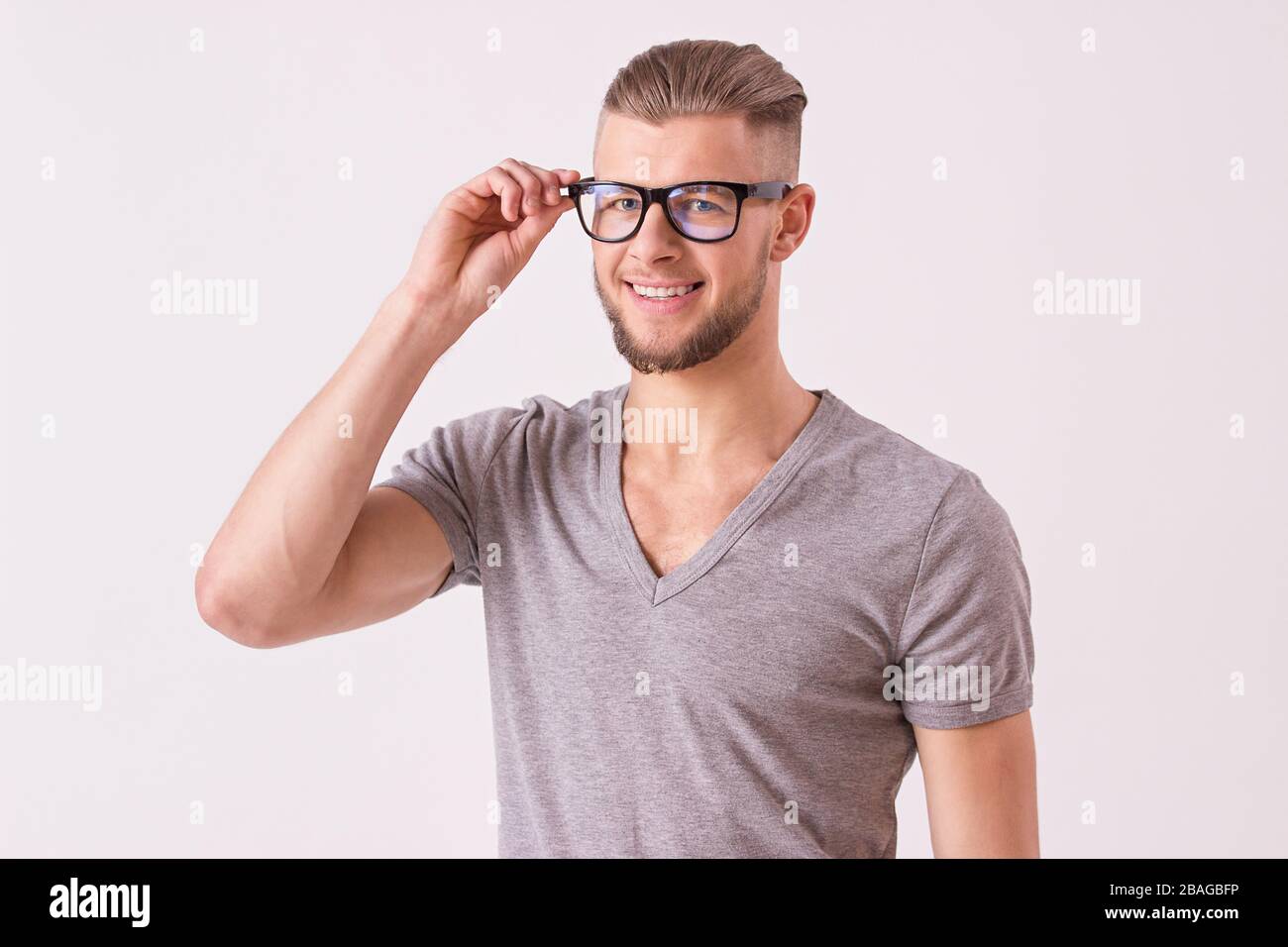 Studio shot of charming young man in t-shirt wearing eyeglasses and smiling while isolated on white background. Charismatic and stylish bearded hipste Stock Photo