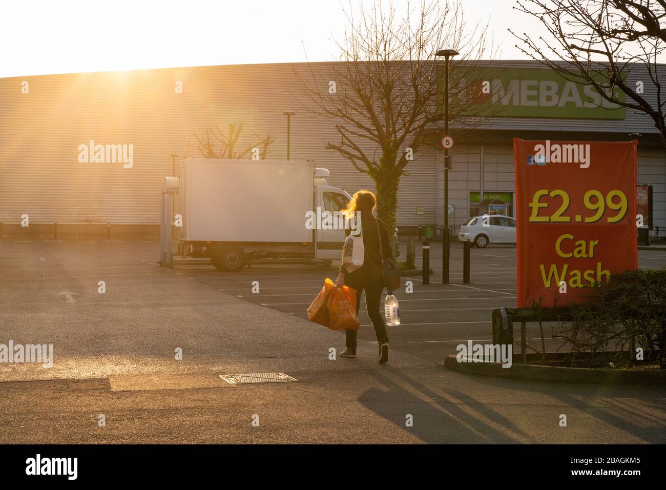 A lone female shopper carries a Sainsbury's orange shopping bag walking past a car wash sign towards Homebase London Stock Photo