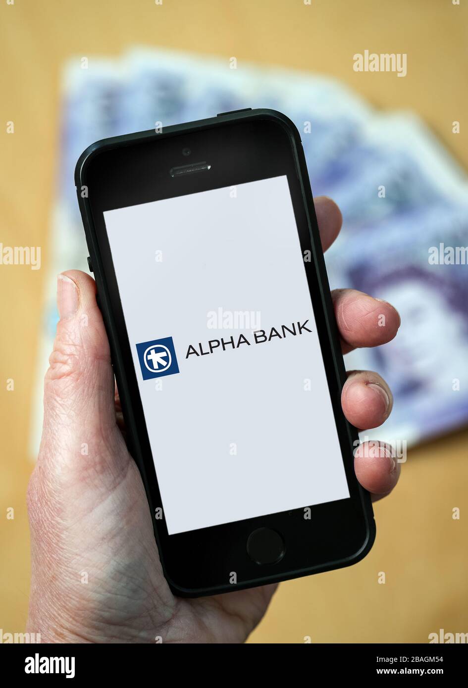 A woman looking at the Alpha Bank logo on a mobile phone. (editorial Use Only) Stock Photo