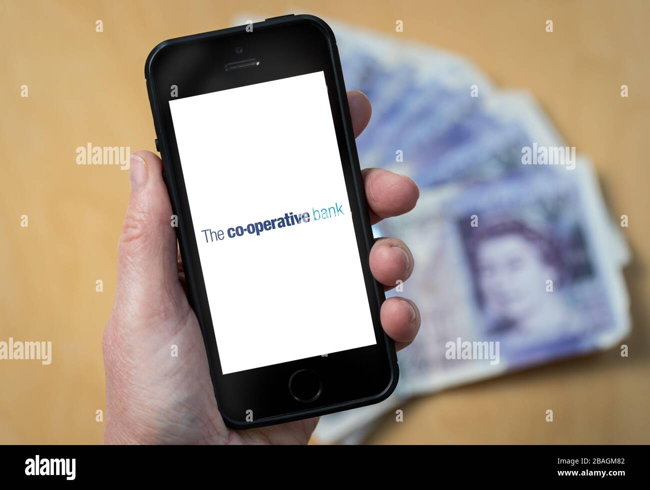 A woman looking at the The Co-operative Bank logo on a mobile phone. (editorial Use Only) Stock Photo