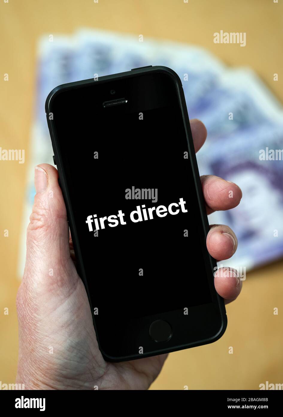 A woman looking at the First Direct Bank logo on a mobile phone. (editorial Use Only) Stock Photo