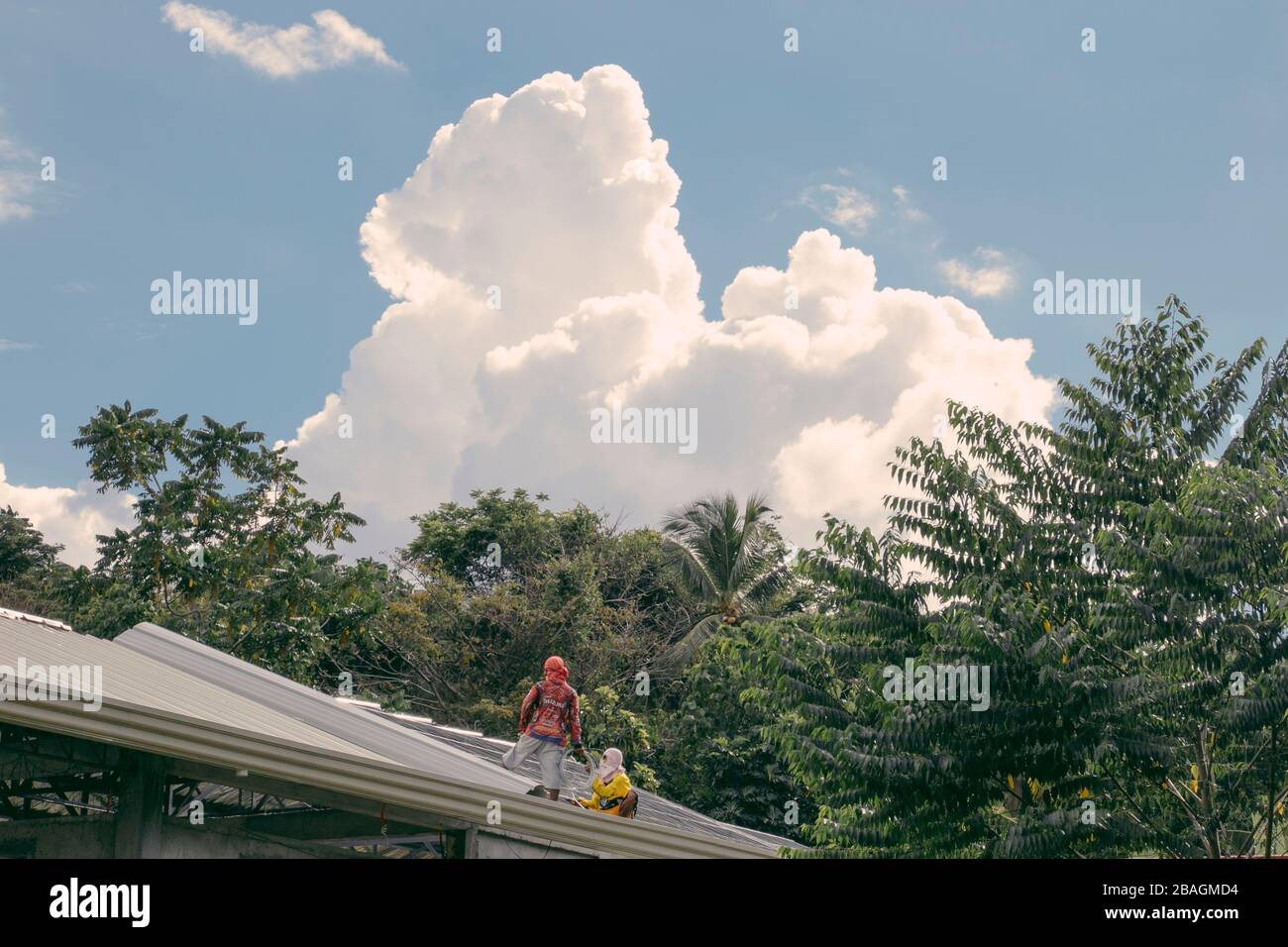 Masked men on top a tin roof outside on a clear day in Samal Island Stock Photo