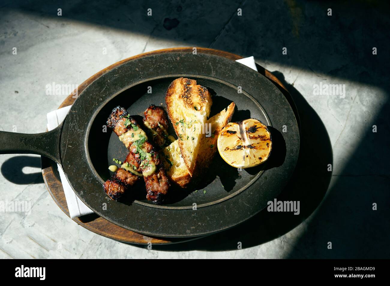 Sausage, toast and lemon on a cast iron plate in the sun. Stock Photo