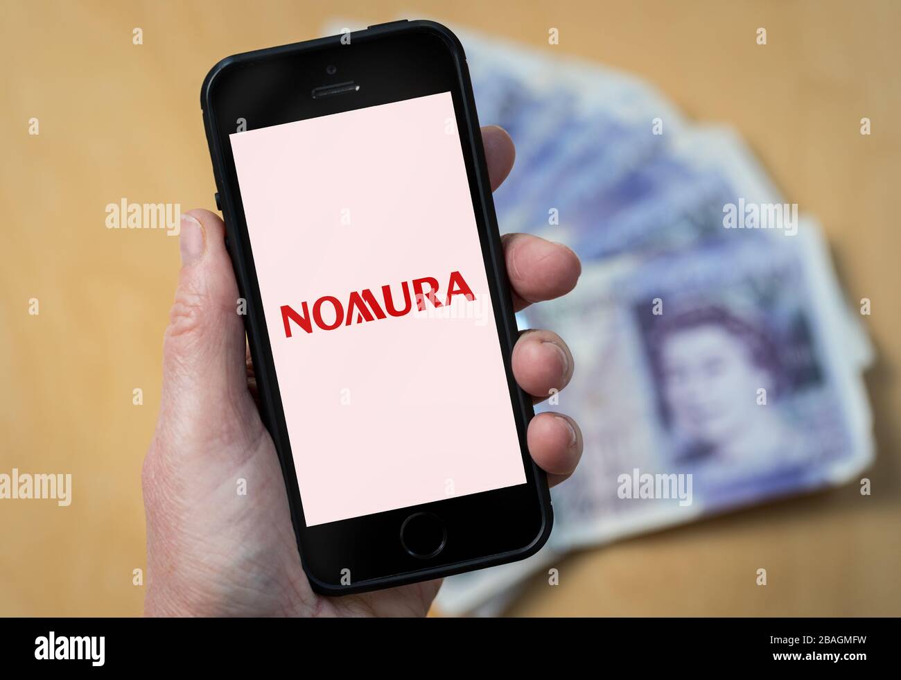 A woman looking at the Nomura Bank logo on a mobile phone. (editorial Use Only) Stock Photo