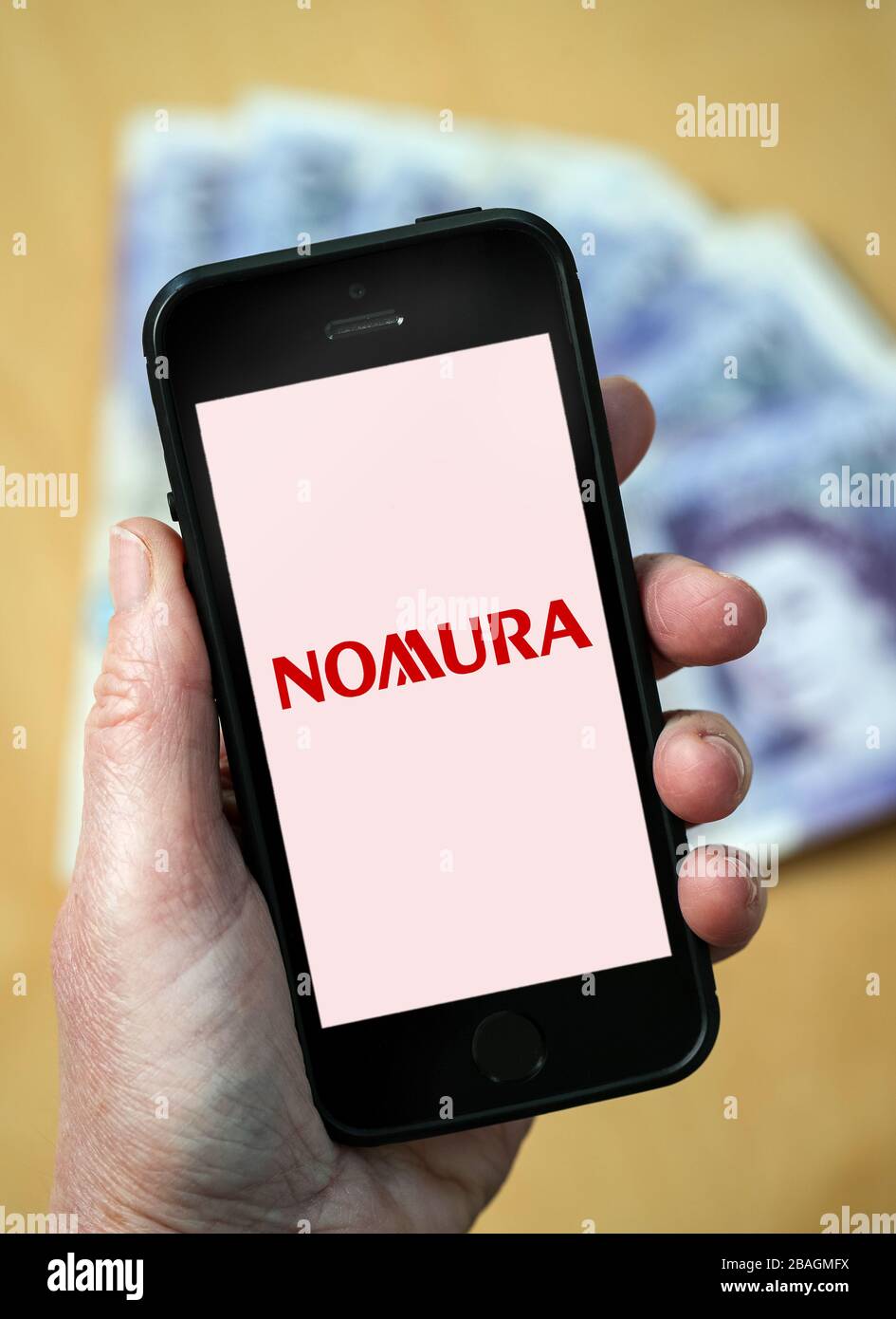 A woman looking at the Nomura Bank logo on a mobile phone. (editorial Use Only) Stock Photo