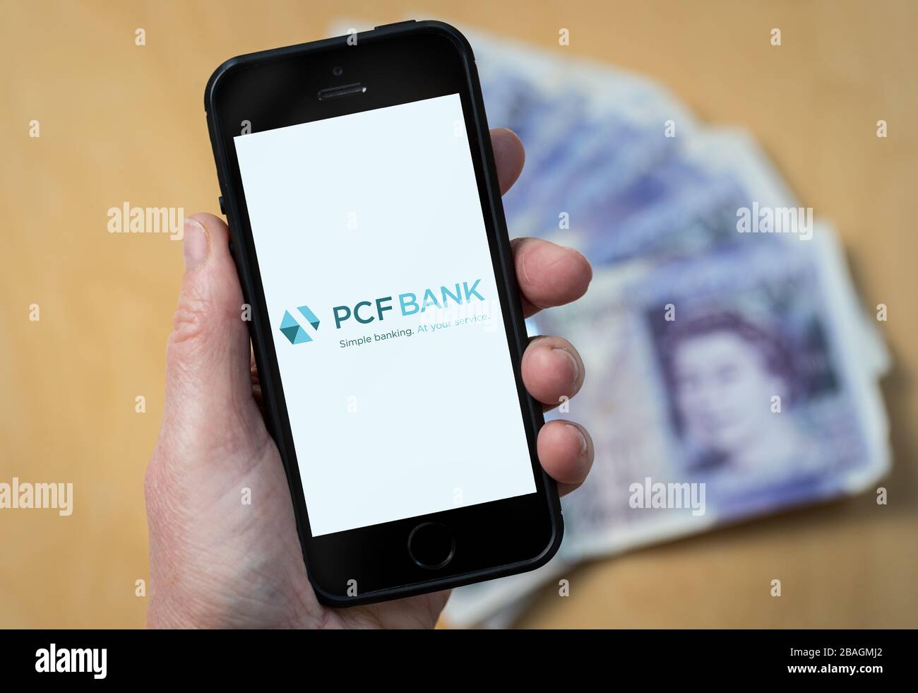 A woman looking at the PCF Bank logo on a mobile phone. (editorial Use Only) Stock Photo