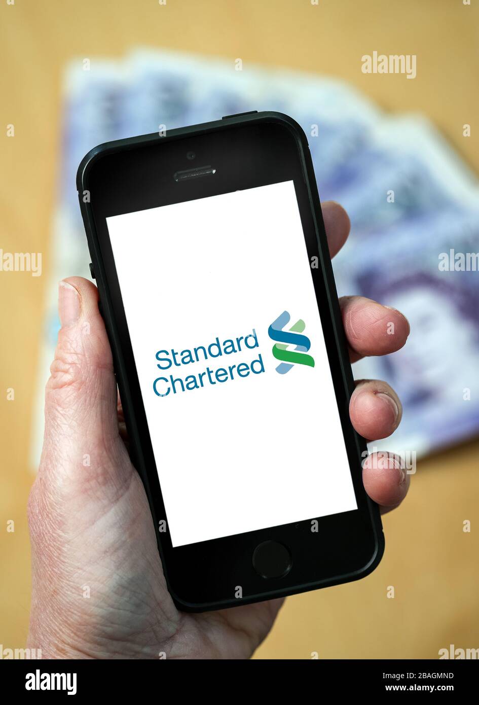 A woman looking at the Standard Chartered Bank logo on a mobile phone. (editorial Use Only) Stock Photo