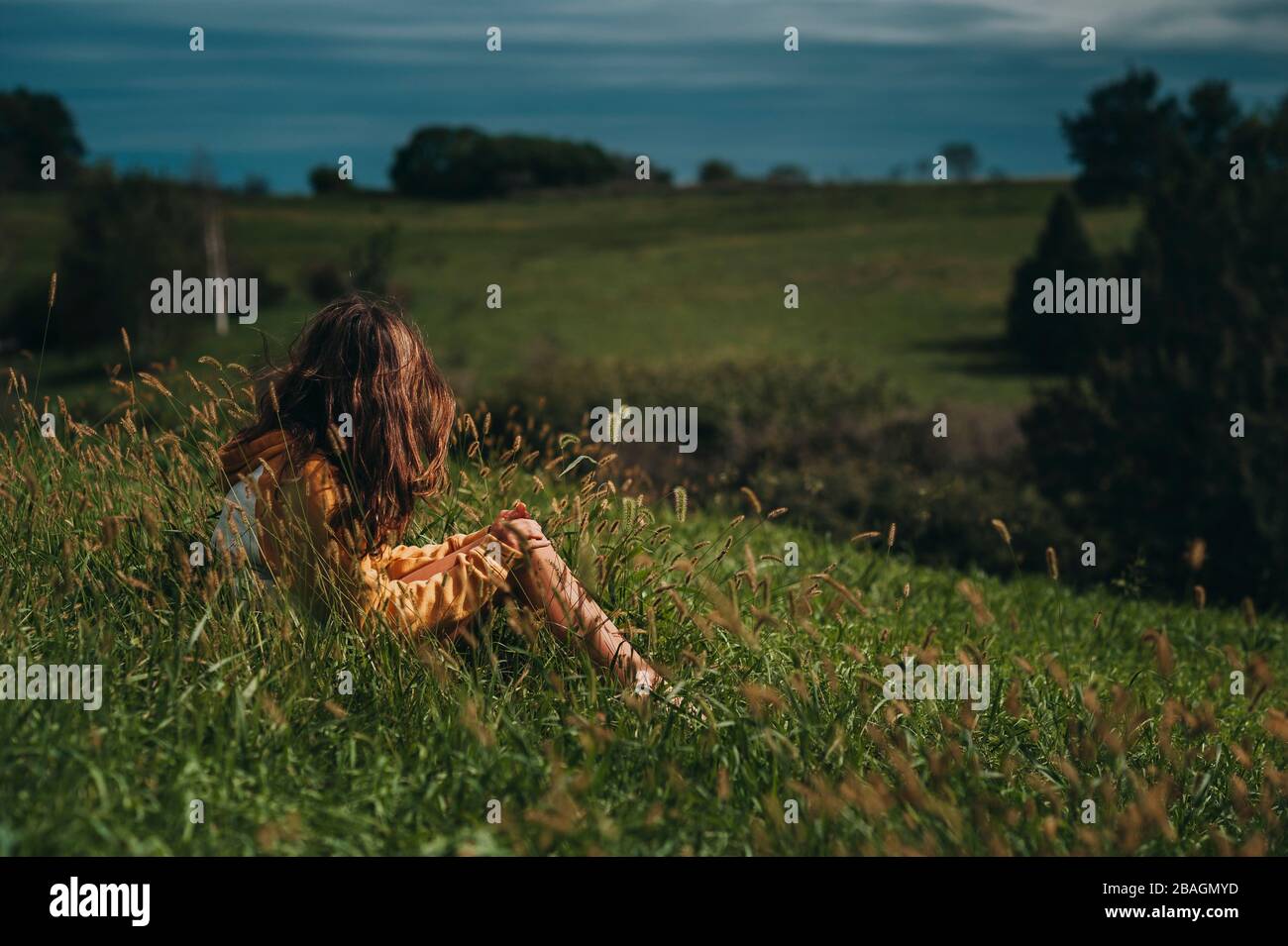 Tween girl looking away at a green hillside with dark skys Stock Photo