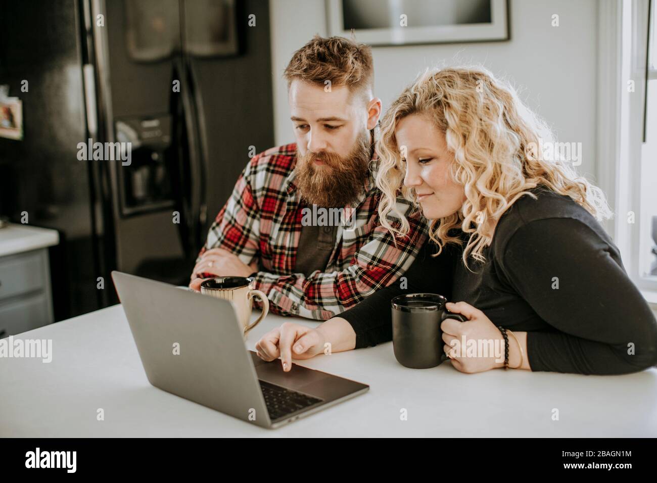 Man and woman couple sit in kitchen with laptop computer and coffee Stock Photo