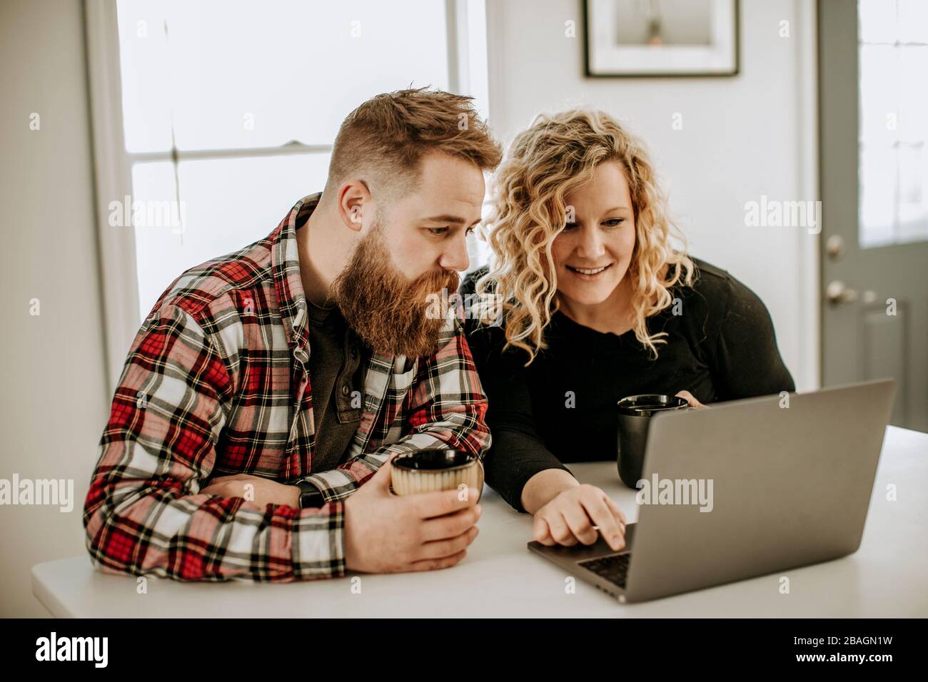 young heterosexual couple sits at table looking at laptop computer Stock Photo