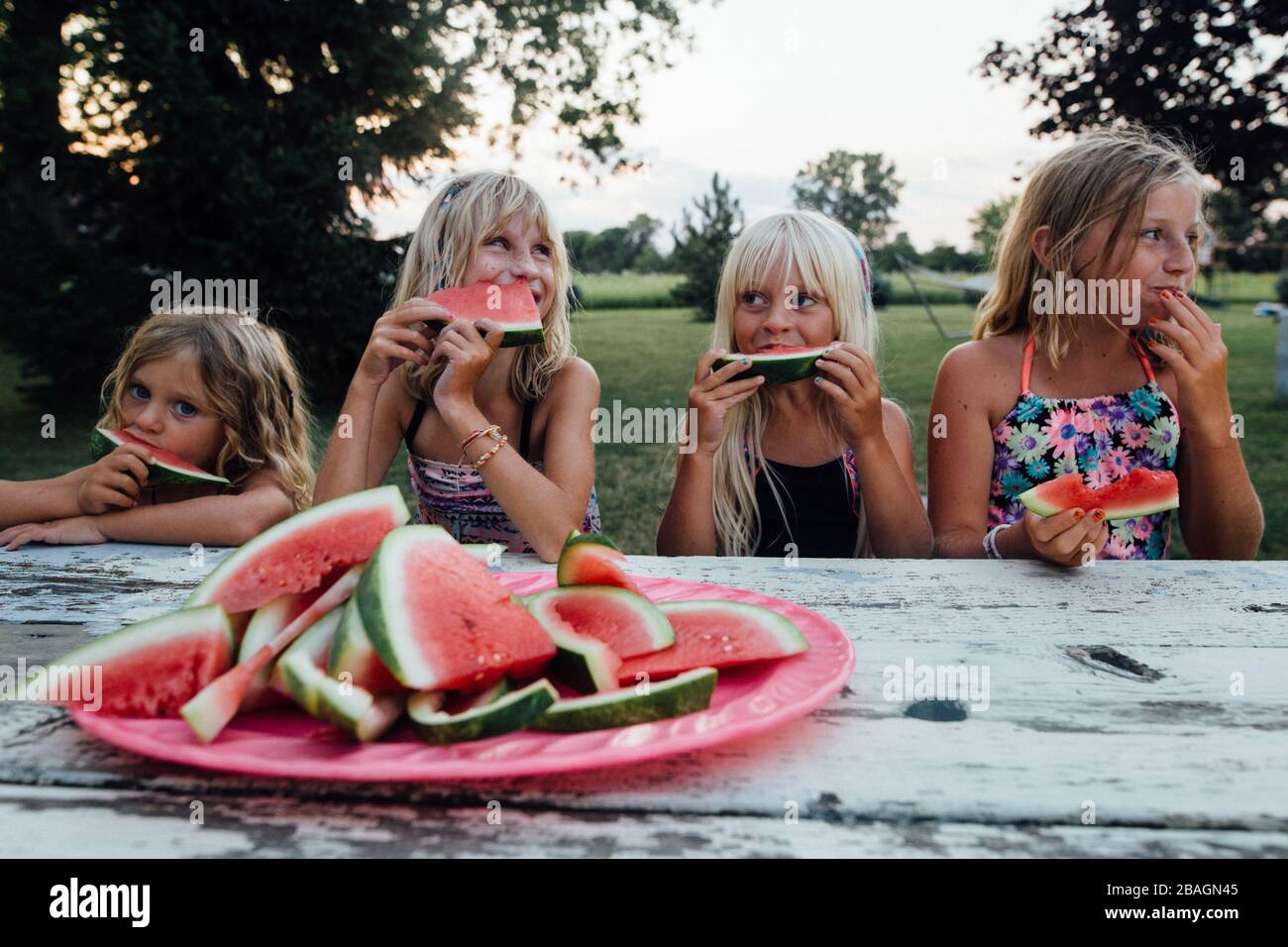 siblings sitting at picnic table outside eating watermelon in summer Stock Photo