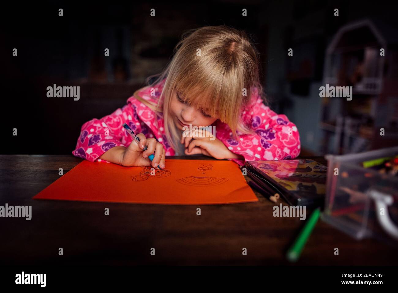 Little blond haired girl drawing a picture at a table on a sunny day Stock Photo