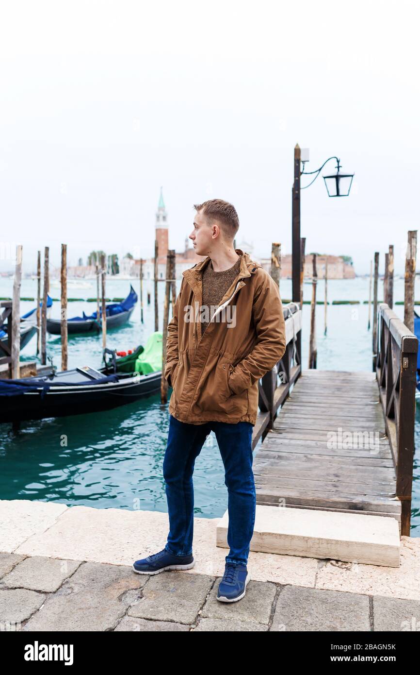 young blond guy in a brown jacket in middle of streets of Venice Stock Photo