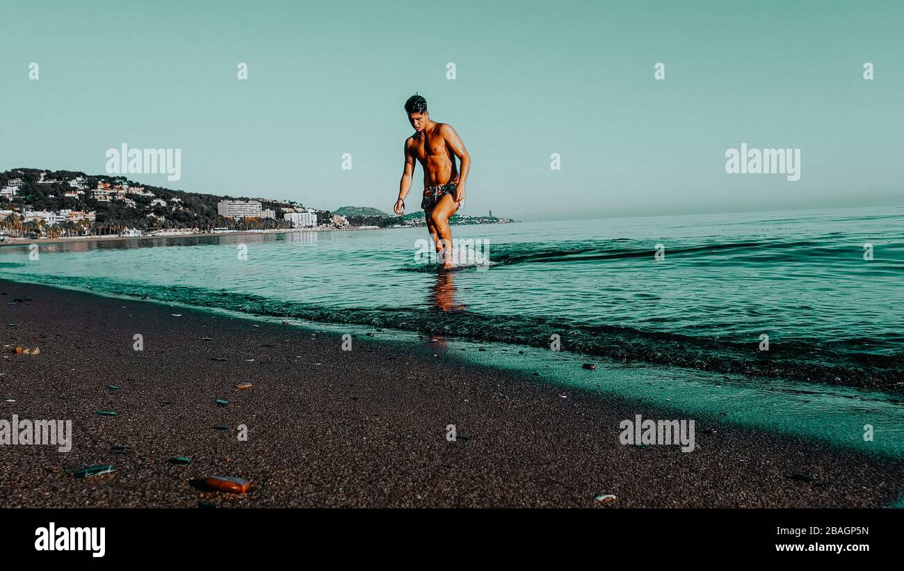 Man model coming out of the water. Alone at the beach. Sunset beach. Stock Photo