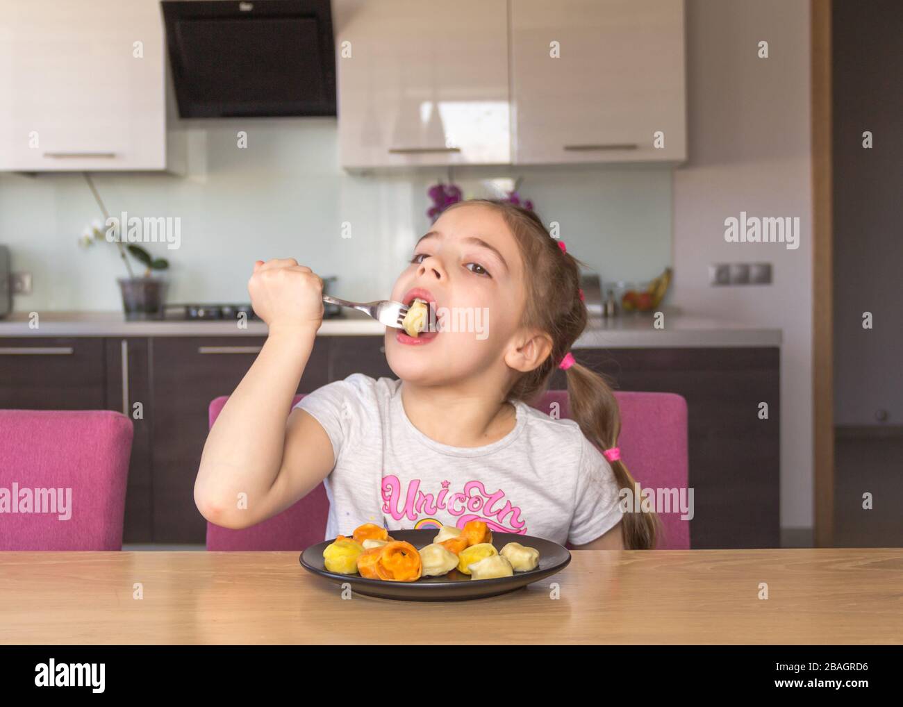 Little girl eats colorful pelmeni. Coronavirus quarantine concept. Stay at home. Stock Photo