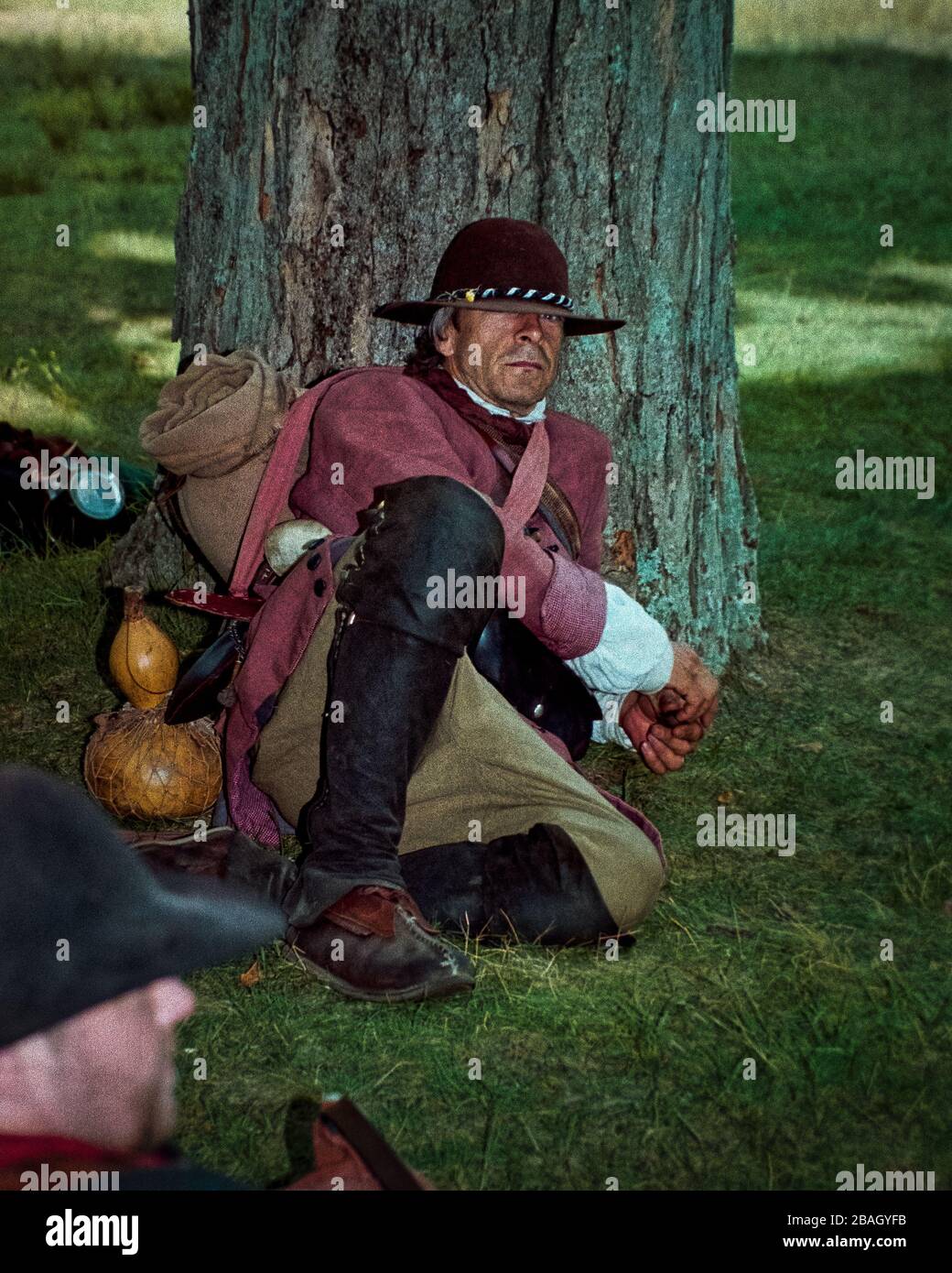 A man dressed as a Minuteman soldier rests at the base of a large tree during the yearly reenactment of the Battles of Lexington and Concord at the Na Stock Photo
