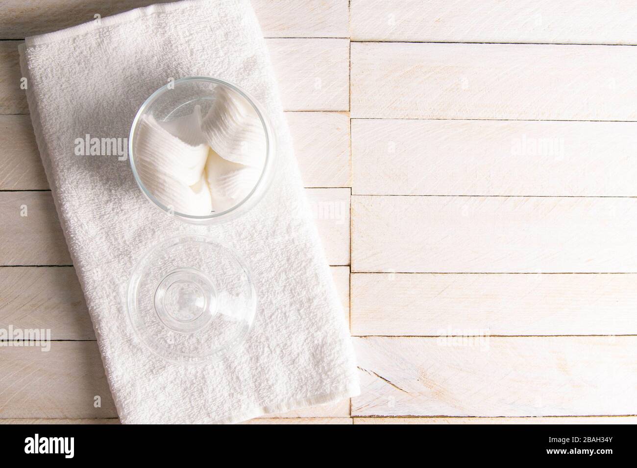Decorative glass jar with cotton pads and towel on table against wooden