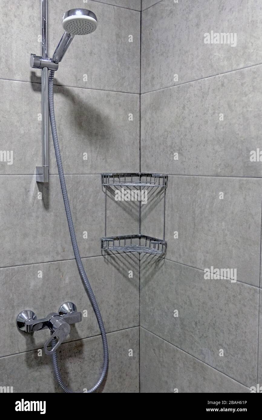 Shower cubicle with gray tiles. Faucet, hose and shower head, corner shelf made of metal rods