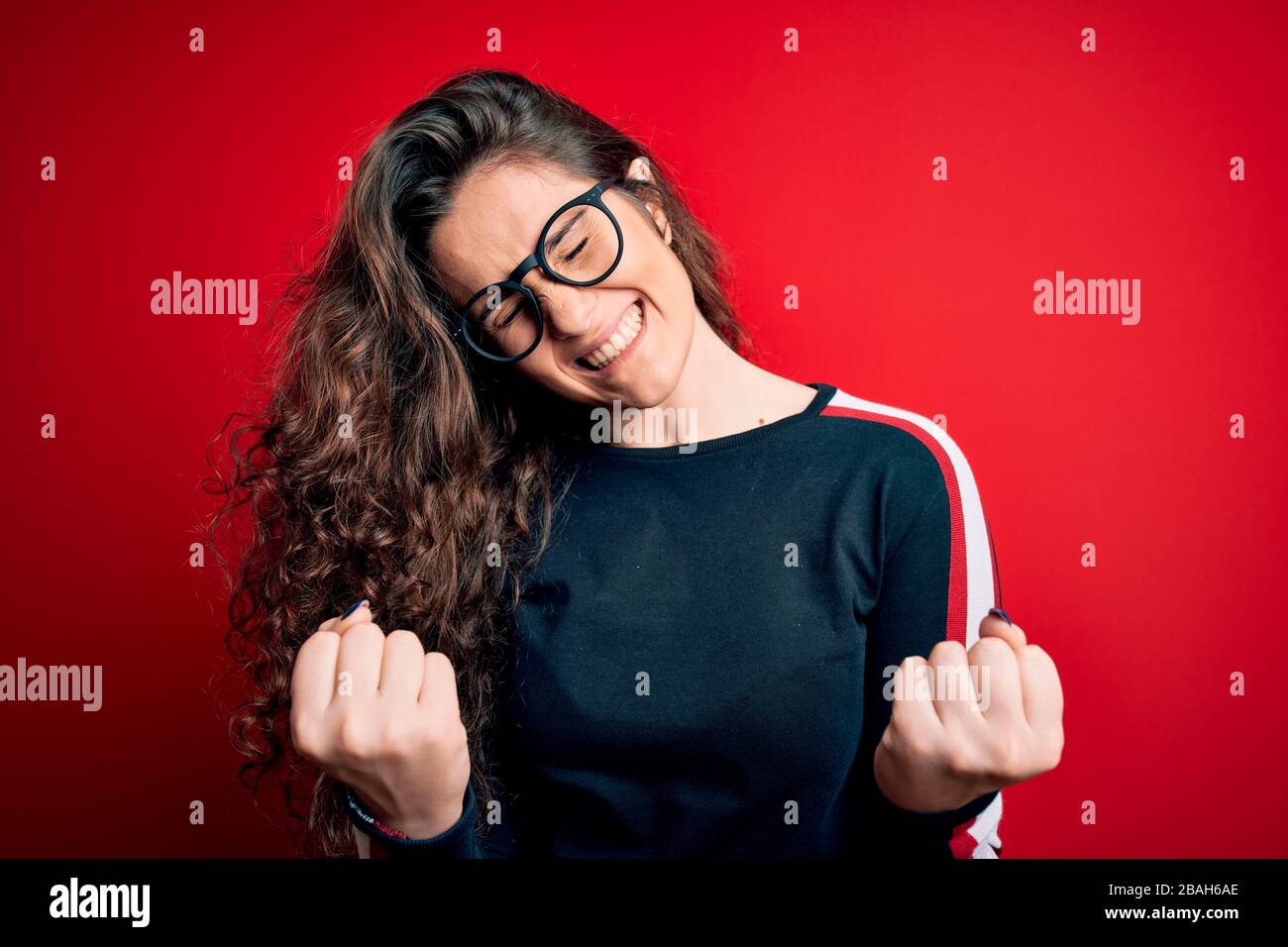 Young beautiful woman with curly hair wearing sweater and glasses over ...