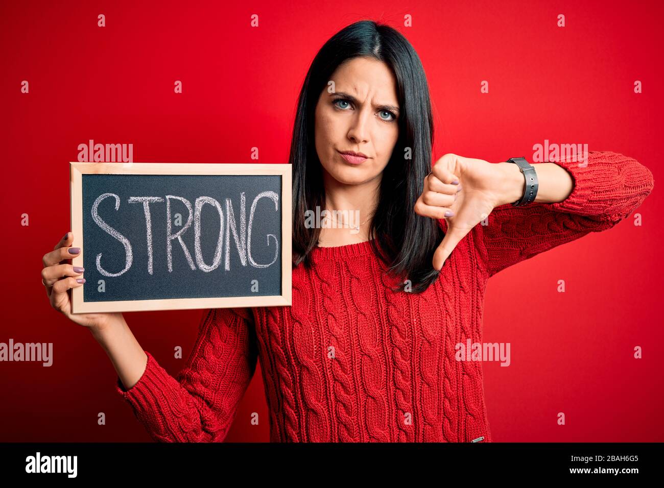 Young brunette woman with blue eyes holding blackboard with strong word ...