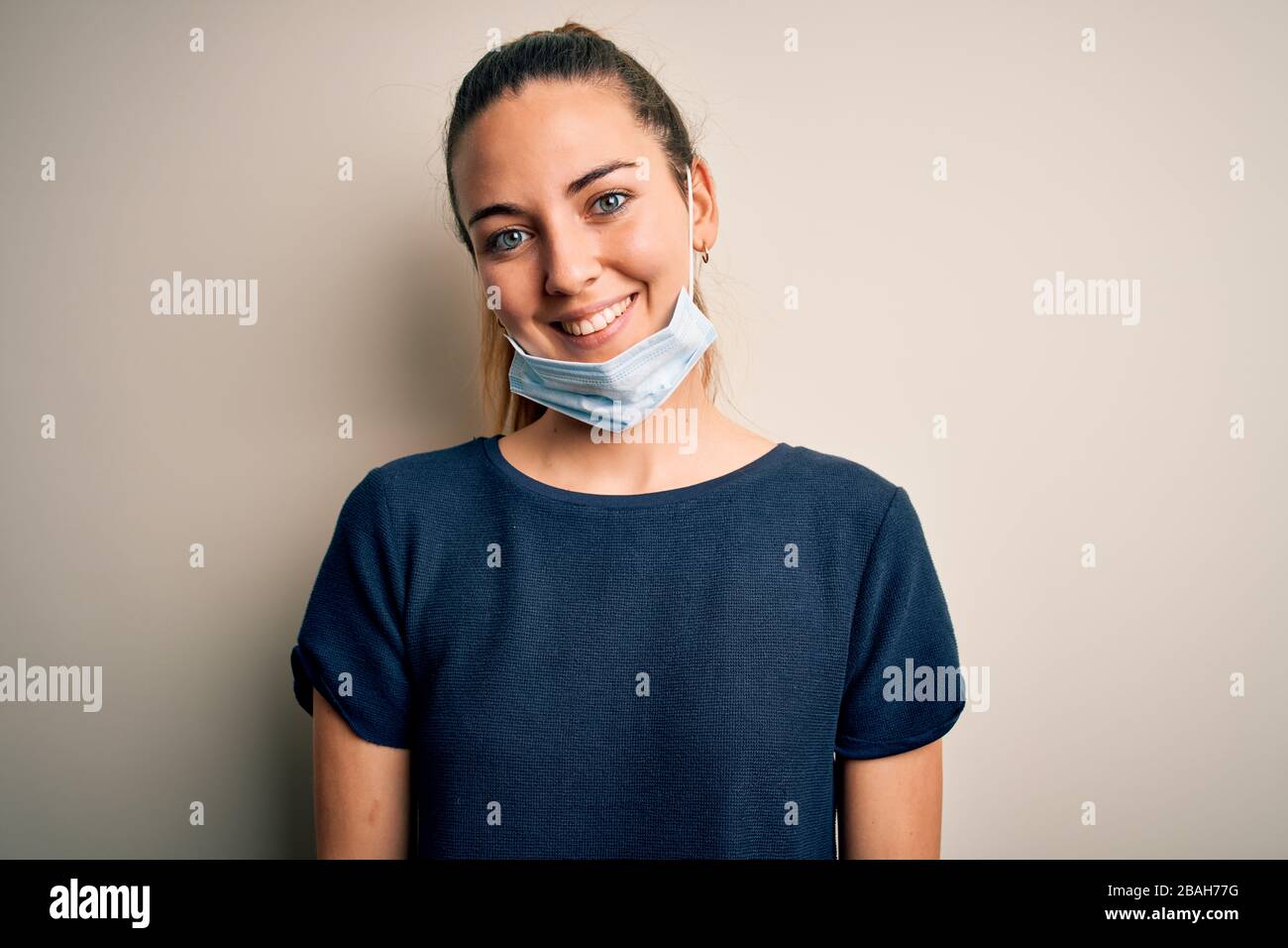 Beautiful blonde woman with blue eyes wearing medical mask over white ...