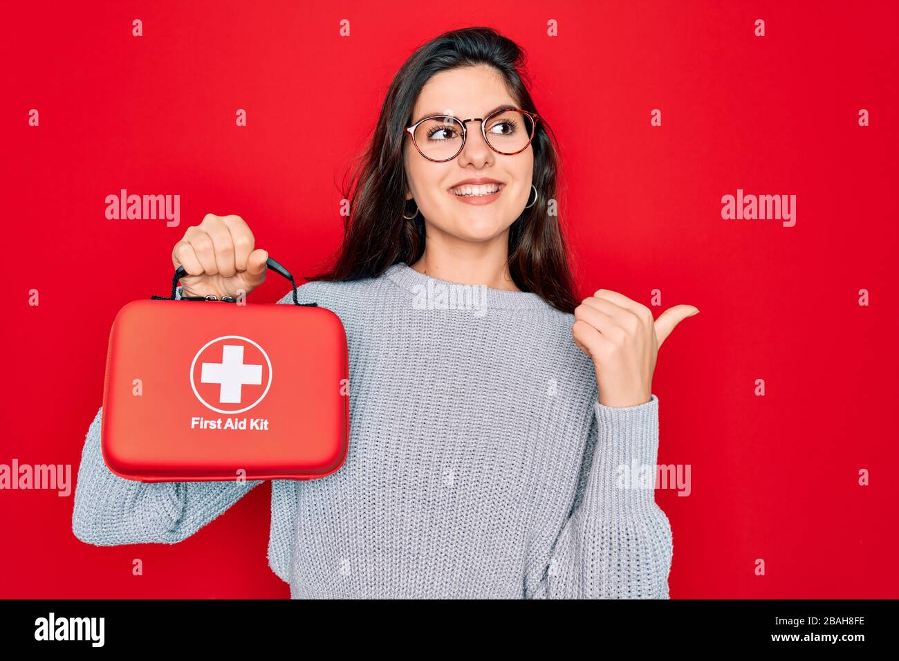 Young beautiful girl holding first aid kit medical box over red ...