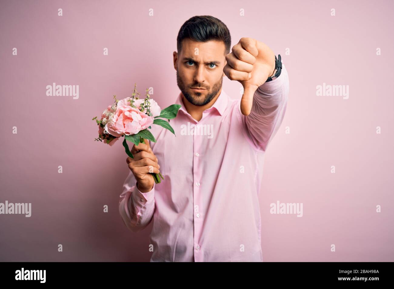 Young romatic man holding bouquet of spring flowers over pink isolatd ...