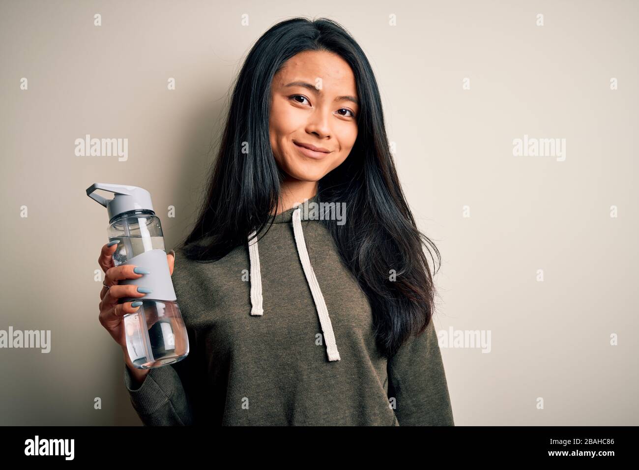 Young beautiful chinese sportswoman holding bottle of water over ...