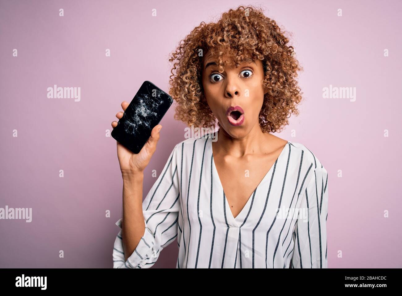 Young african american curly woman holding broken smartphone showing ...