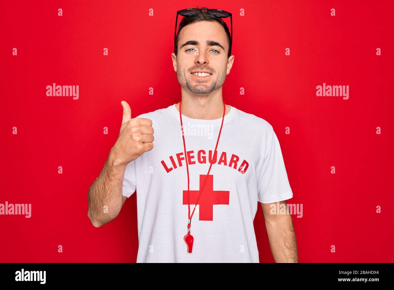 Handsome lifeguard man wearing t-shirt with red cross and whistle over ...