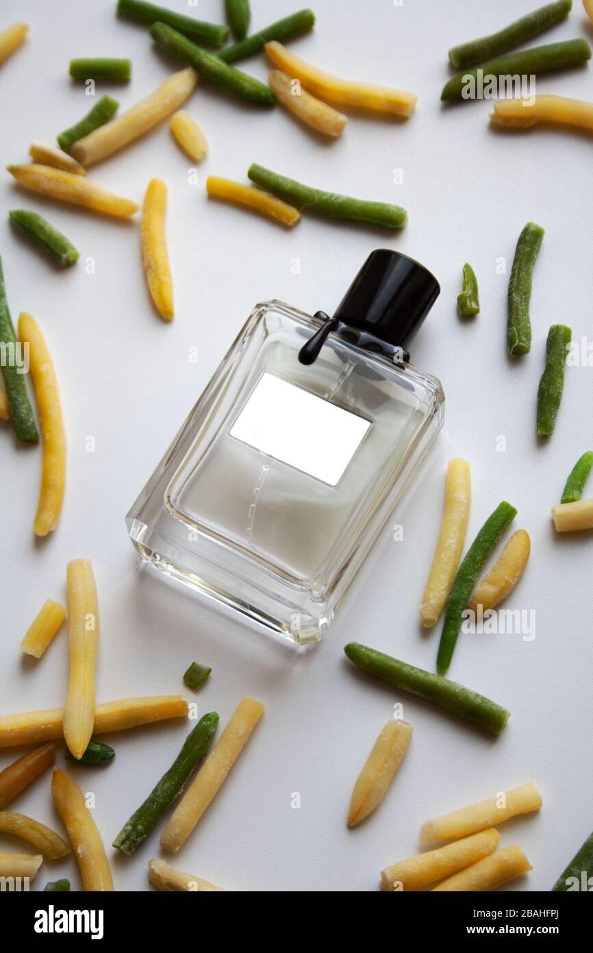 Glass perfume bottle in a pile of green and yellow bean pods on white background Stock Photo