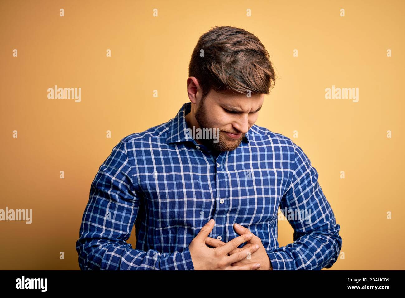 Young blond businessman with beard and blue eyes wearing shirt over yellow background with hand on stomach because indigestion, painful illness feelin Stock Photo