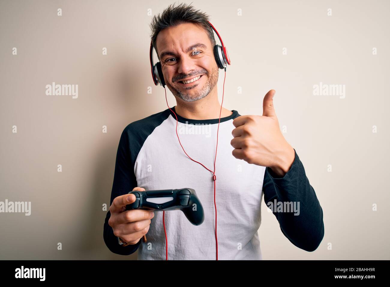 Young handsome gamer man playing video game using joystick and headphones  happy with big smile doing ok sign, thumb up with fingers, excellent sign  Stock Photo - Alamy