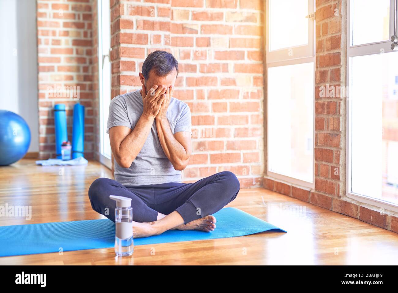 Middle age handsome sportman sitting on mat doing stretching yoga exercise  at gym with sad expression covering face with hands while crying. Depressio  Stock Photo - Alamy