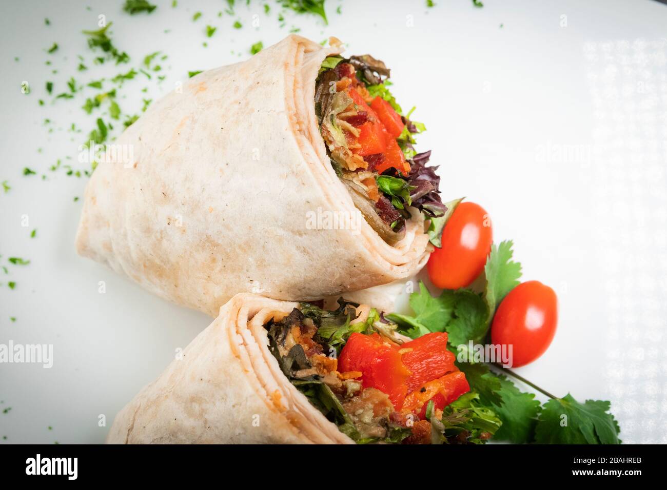 A fresh tasty turkey wrap displayed on white platter with chopped parsley garnish Stock Photo