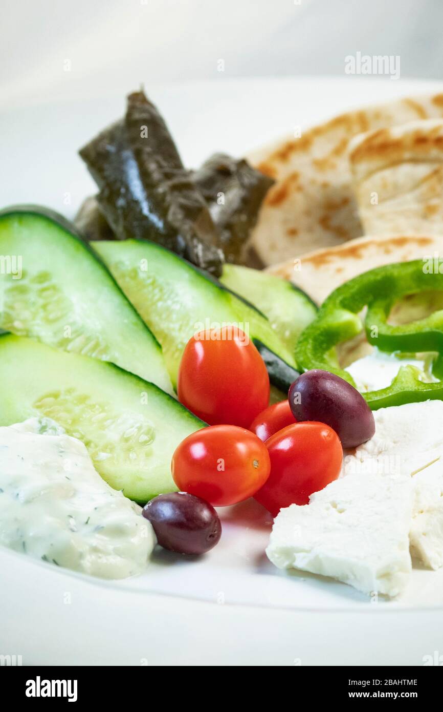 Shallow focus view of simple Greek meze food platter; with vegetables, pita, feta, and grape leaves Stock Photo