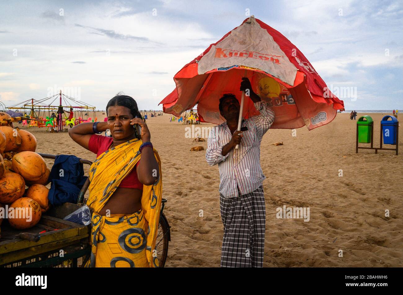 Man opening an umbrella while his wife talks on the phone, Marina Beach, Chennai, India Stock Photo