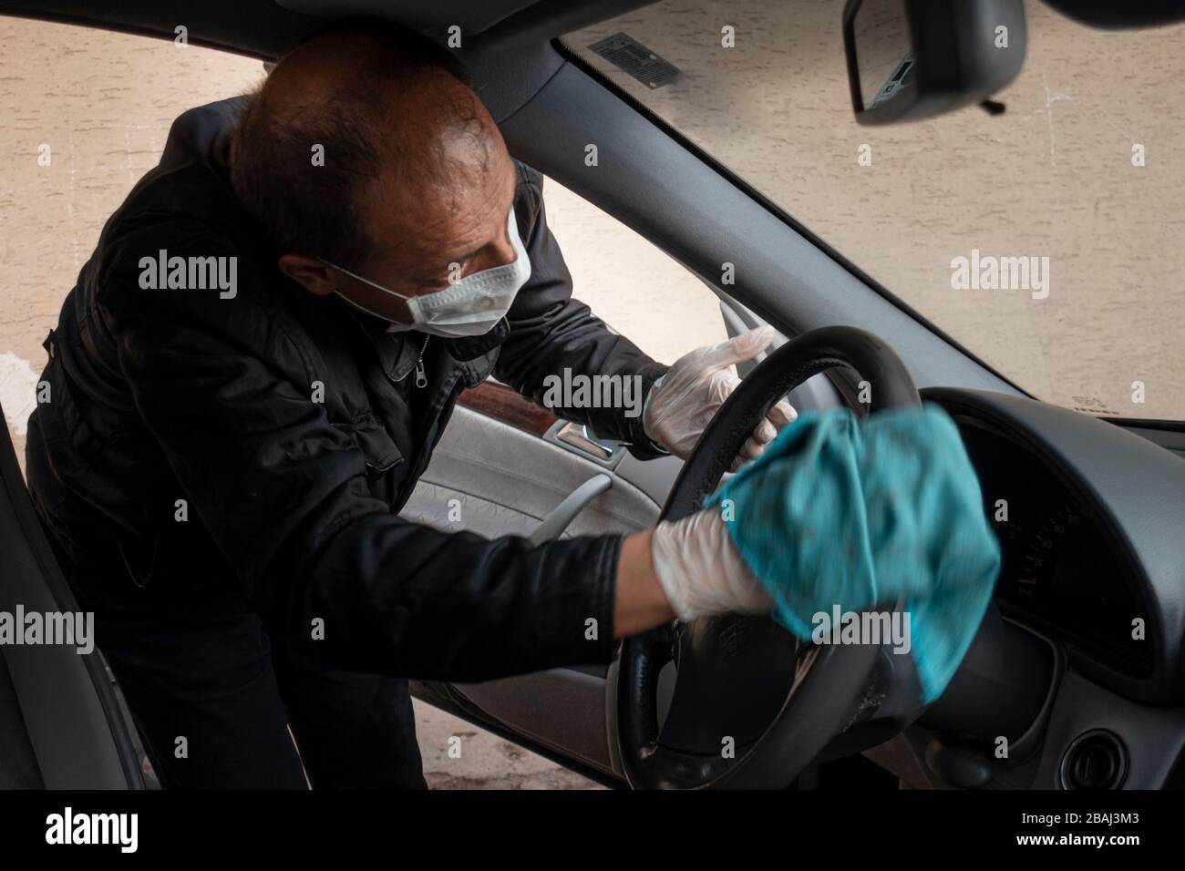 Middle aged Turkish man disinfects his car as a precaution for the pandemic corona virus Stock Photo