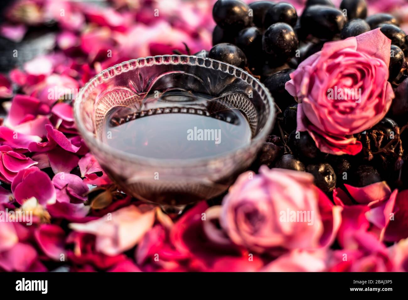 Close up shot of a raw fresh bunch of grapes with some red and pink roses flowers with it on black wooden board. Stock Photo