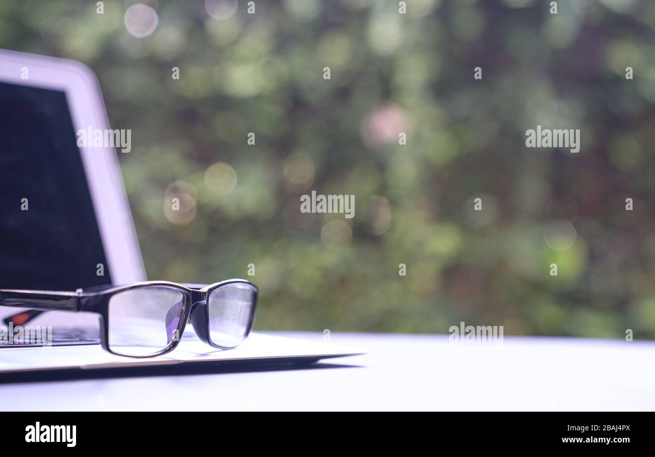 Computer laptop with reading glasses and green nature background. Work remotely or from home. Copy space. Stock Photo